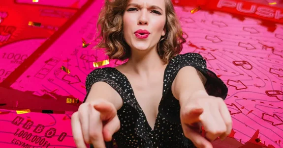 Fiatal nő előre mutatva a kamerába, mögötte kaparós sorsjegyek és konfetti piros színvilágban