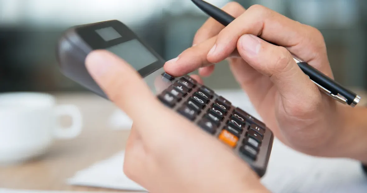 Kézben tartott számológép és toll, a nyereményadó mértékének pénzügyi számítását ábrázolva