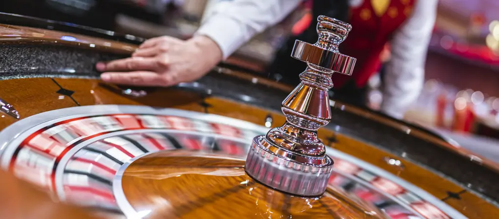 Rulettker&eacute;k mozg&aacute;s k&ouml;zben, az oszt&oacute; keze a peremen, h&aacute;tt&eacute;rben a kaszin&oacute; f&eacute;nyeivel